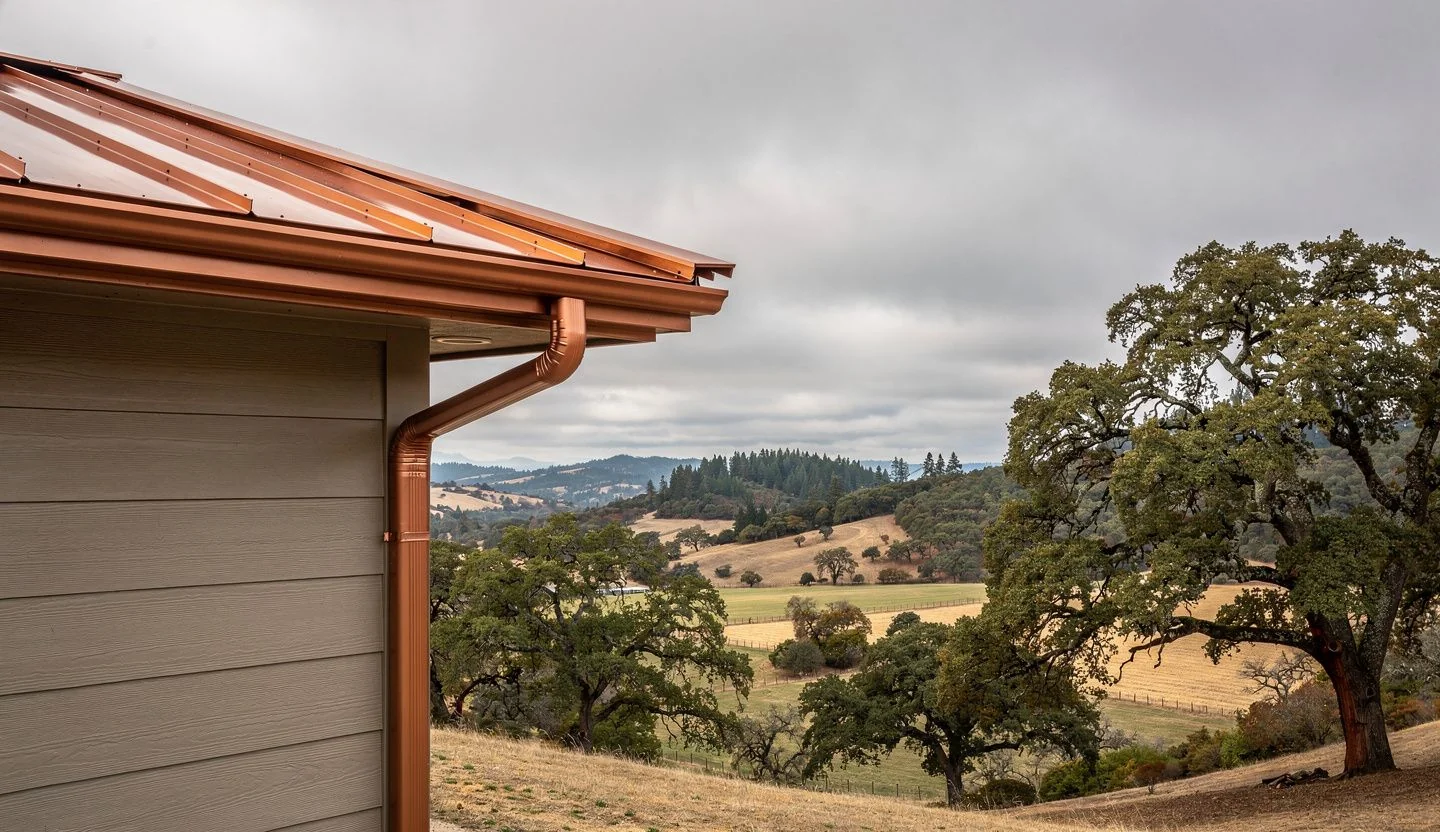 Seamless copper-toned gutters on hillside rural home in Melrose Oregon with rolling farmland and mixed forest
